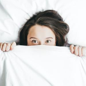 Woman in bed holding covers over her face